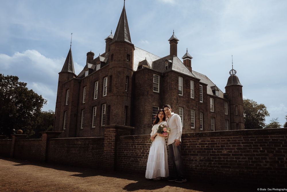 Bride and groom embracing in front of a historic brick castle under a blue sky on their wedding day.