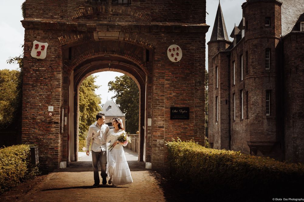 Bride and groom embrace under a castle archway on their wedding day, surrounded by lush greenery.