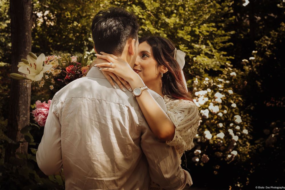 Couple sharing a romantic moment in a lush garden with blooming flowers, woman smiling as she touches mans face.