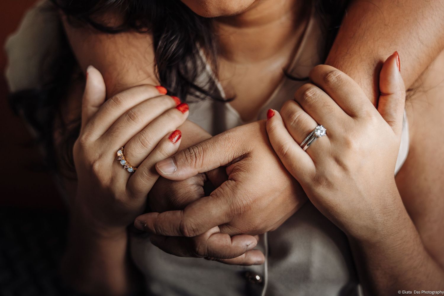 Close-up of two women embracing with hands clasped, red manicured nails and a diamond engagement ring on one finger.