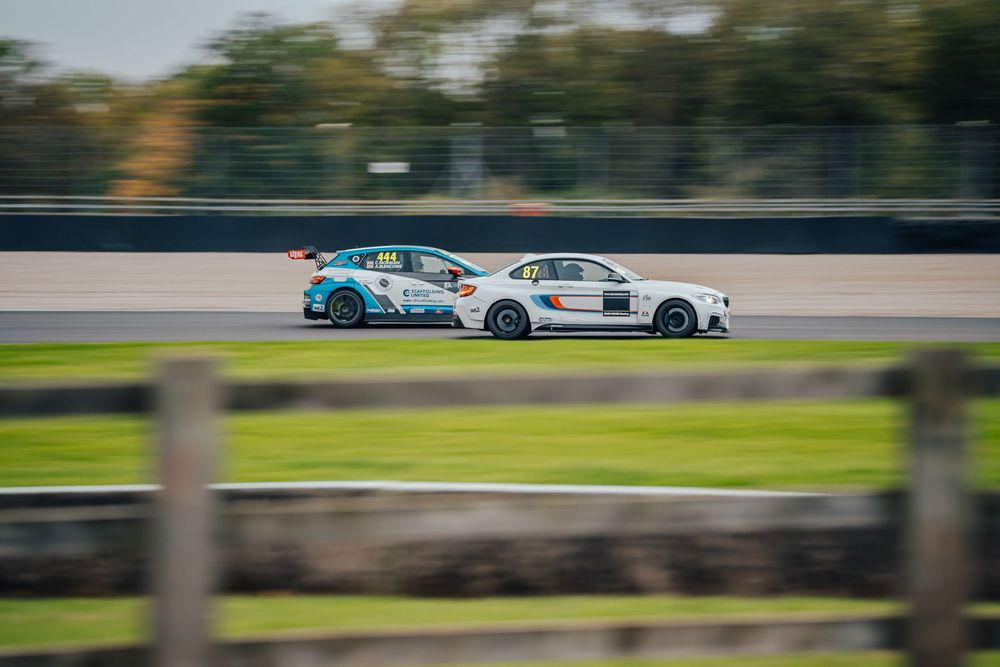 High-performance race cars navigate a curve on a professional racing circuit surrounded by green landscape.