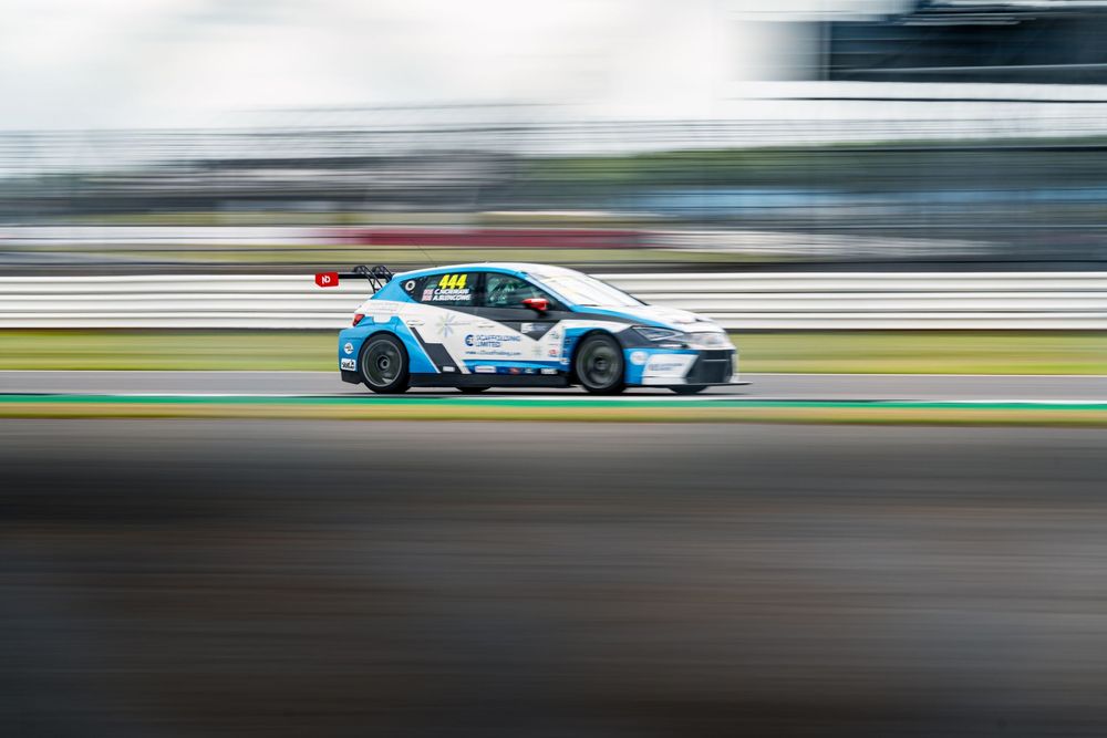 Race cars blur past the camera during a high-speed motorsport competition on a professional track.