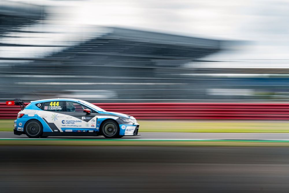Blue and white race car speeds past on a racetrack with motion blur effect.