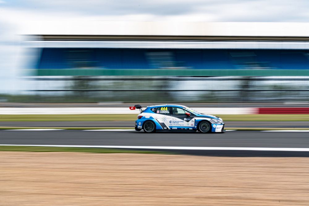 A blue and white racing car speeds past on a racetrack with motion blur effect in the background.