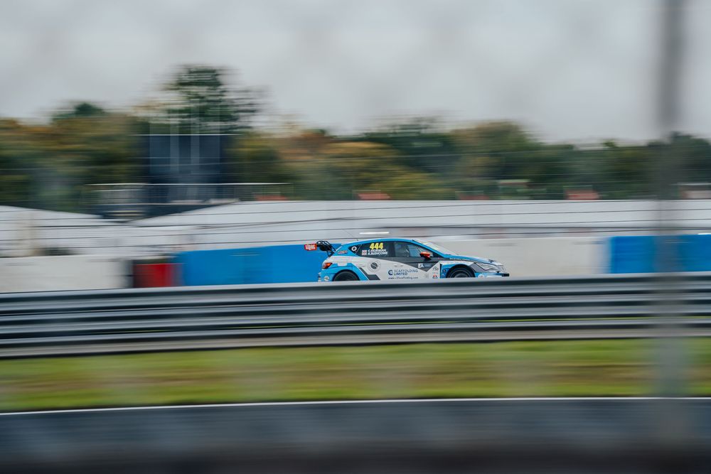 Race cars speed through a curving racetrack on a cloudy day during a motorsport competition.
