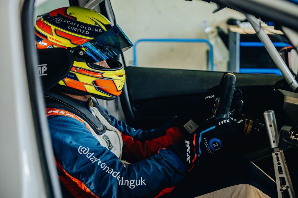 Racing driver in the cockpit wearing a colorful helmet with yellow and red designs.