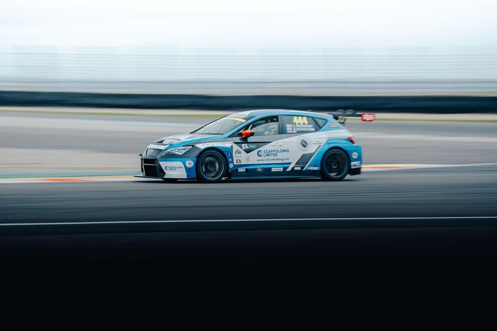 Blue and white race cars speed along a motorsport track during a competitive racing event.