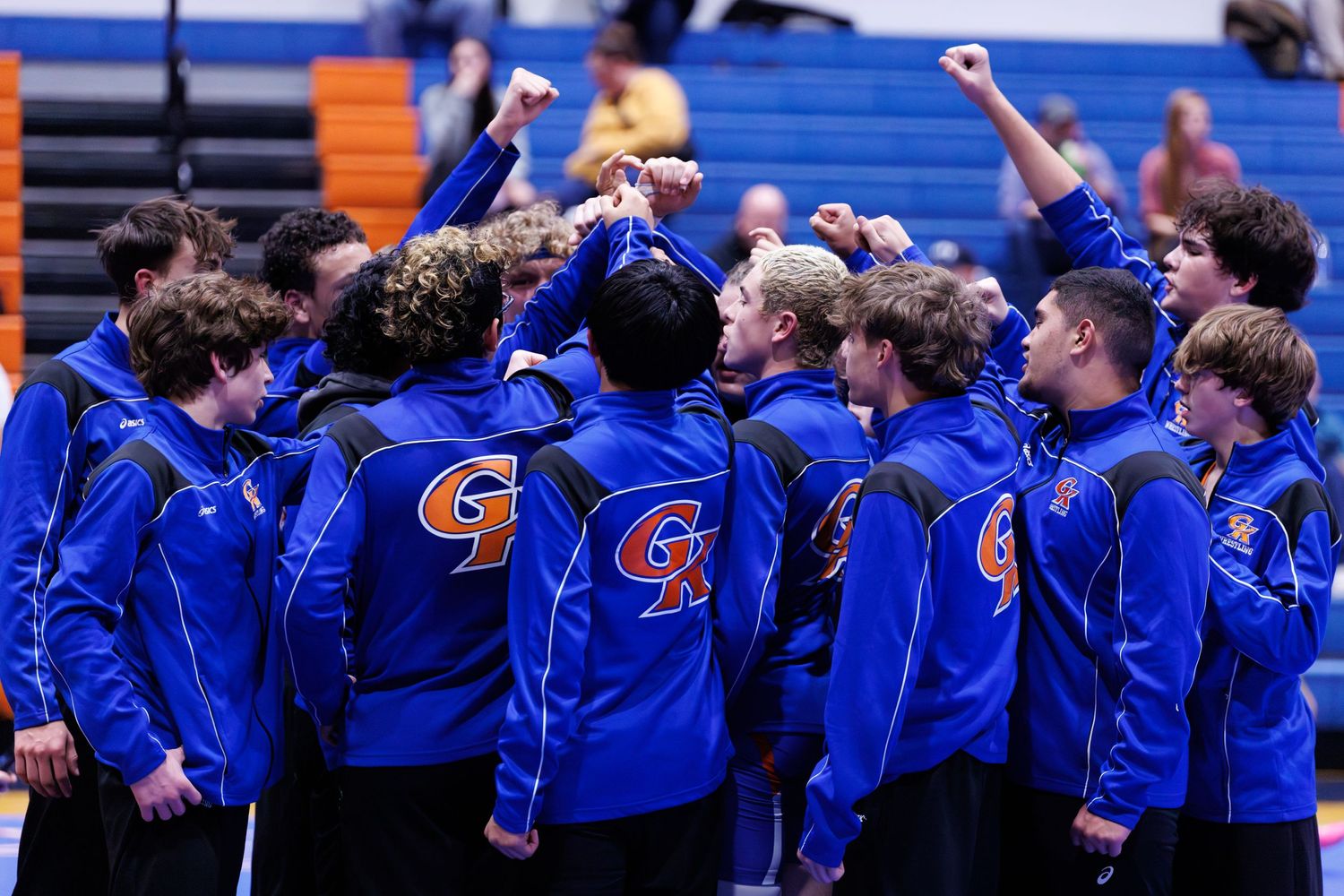 Athletes in blue jackets stand in a row with raised fists during a team celebration.