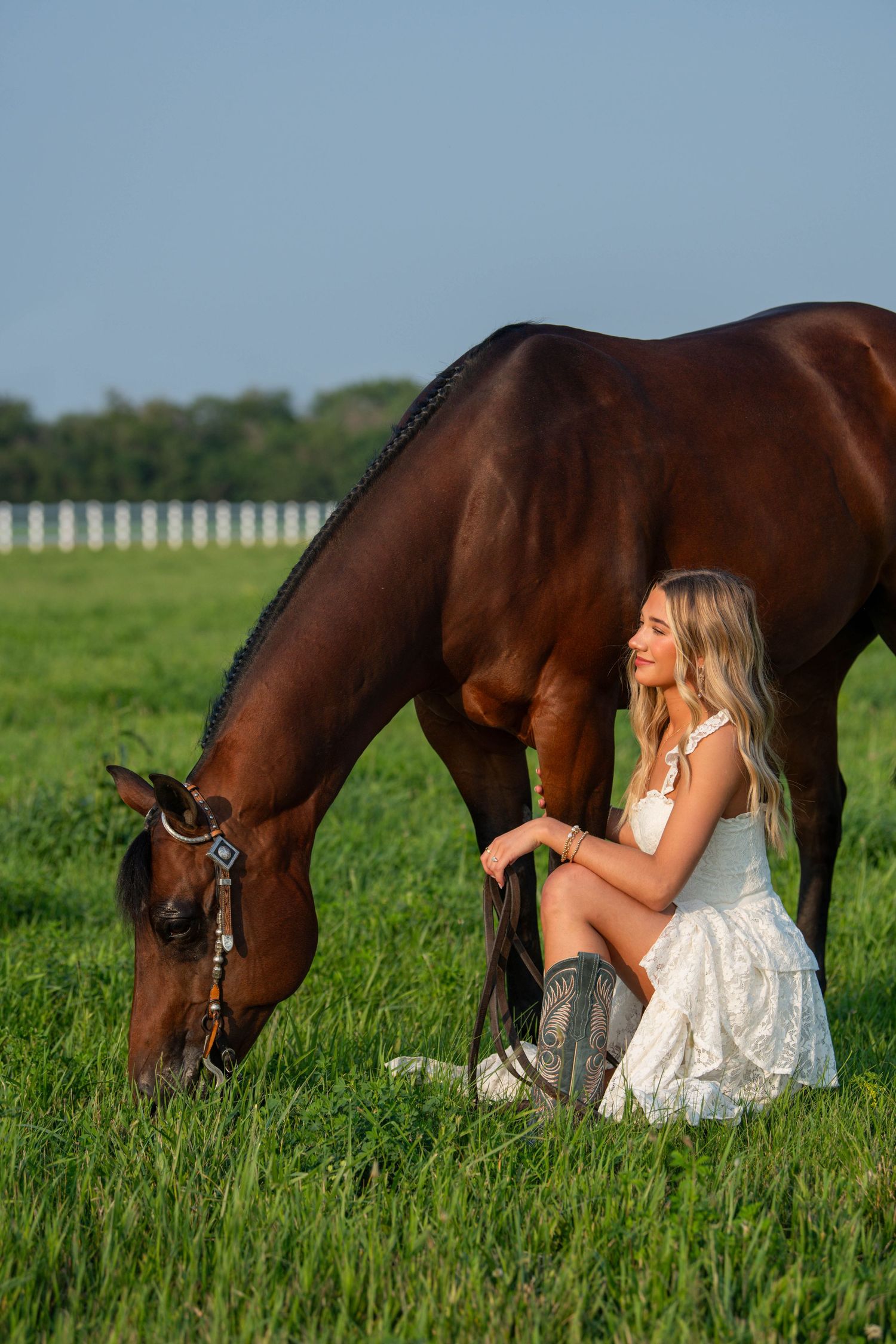 Horse and companion resting together in green spring meadow with white fence backdrop.