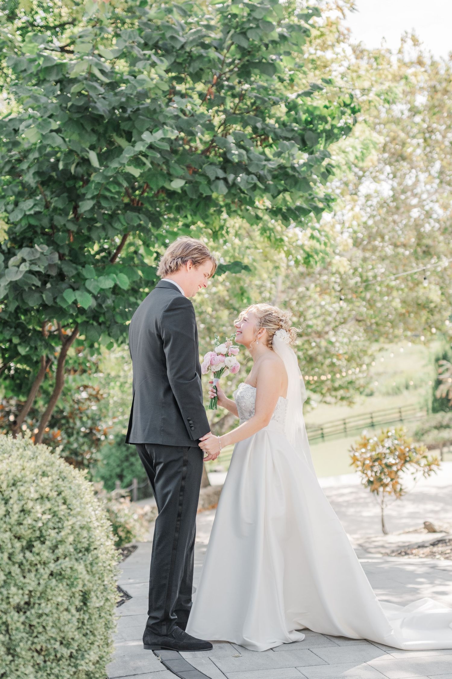 A couple shares an intimate moment on their wedding day on a paved garden path.