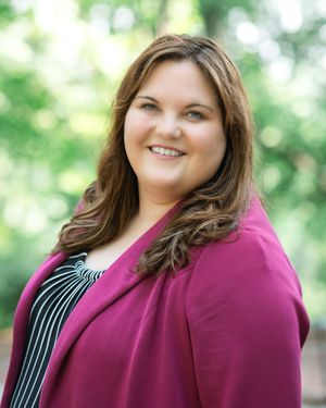 Professional headshot against blurred green background featuring magenta blazer and striped top.