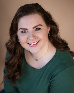 Portrait of someone wearing a dark green sweater smiling warmly against a neutral background.