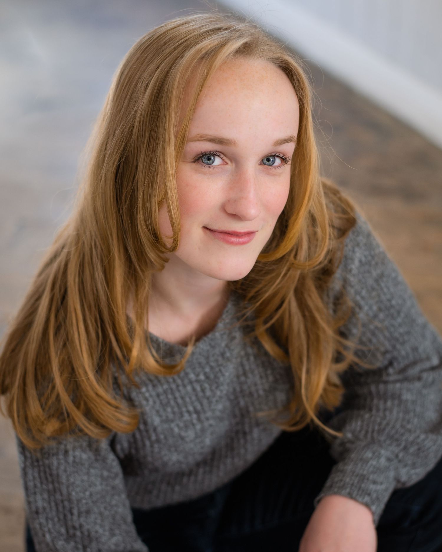 A person with long red hair wearing a grey sweater leans forward in a series of candid poses.