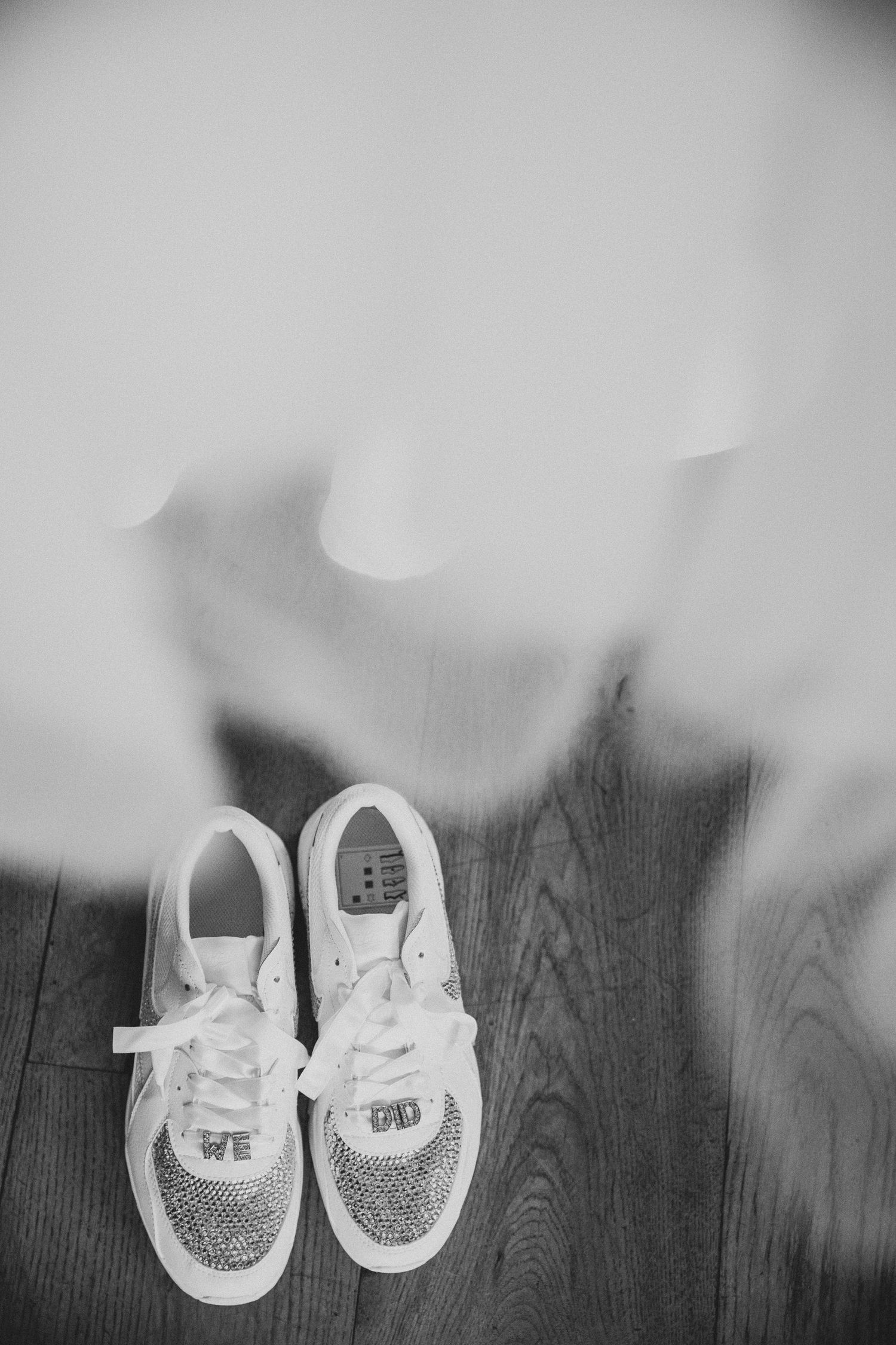 A pair of white glittery bridal shoes arranged on a dark wooden floor with soft focus edges.