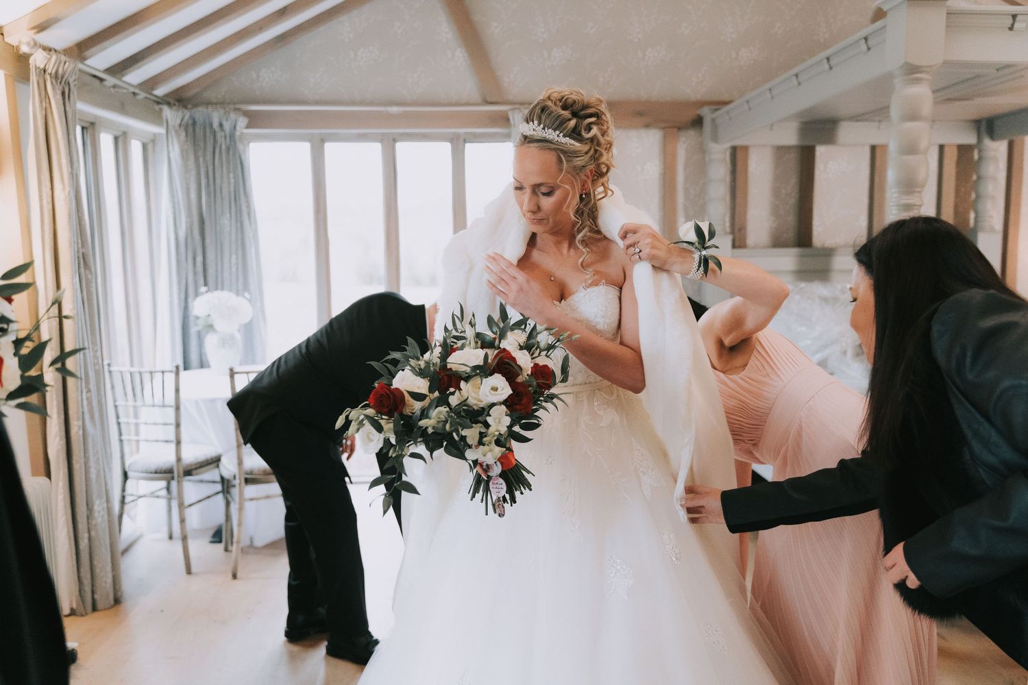 Wedding party members in formal attire gather together in a bright indoor venue during a celebration.