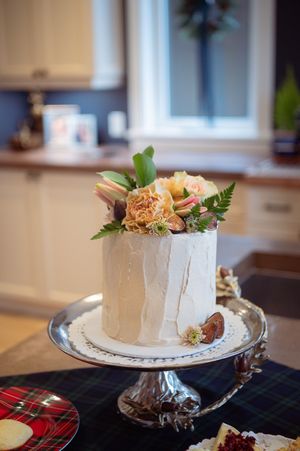 White frosted layer cake decorated with fresh herbs and garnishes displayed on an elegant silver cake stand.