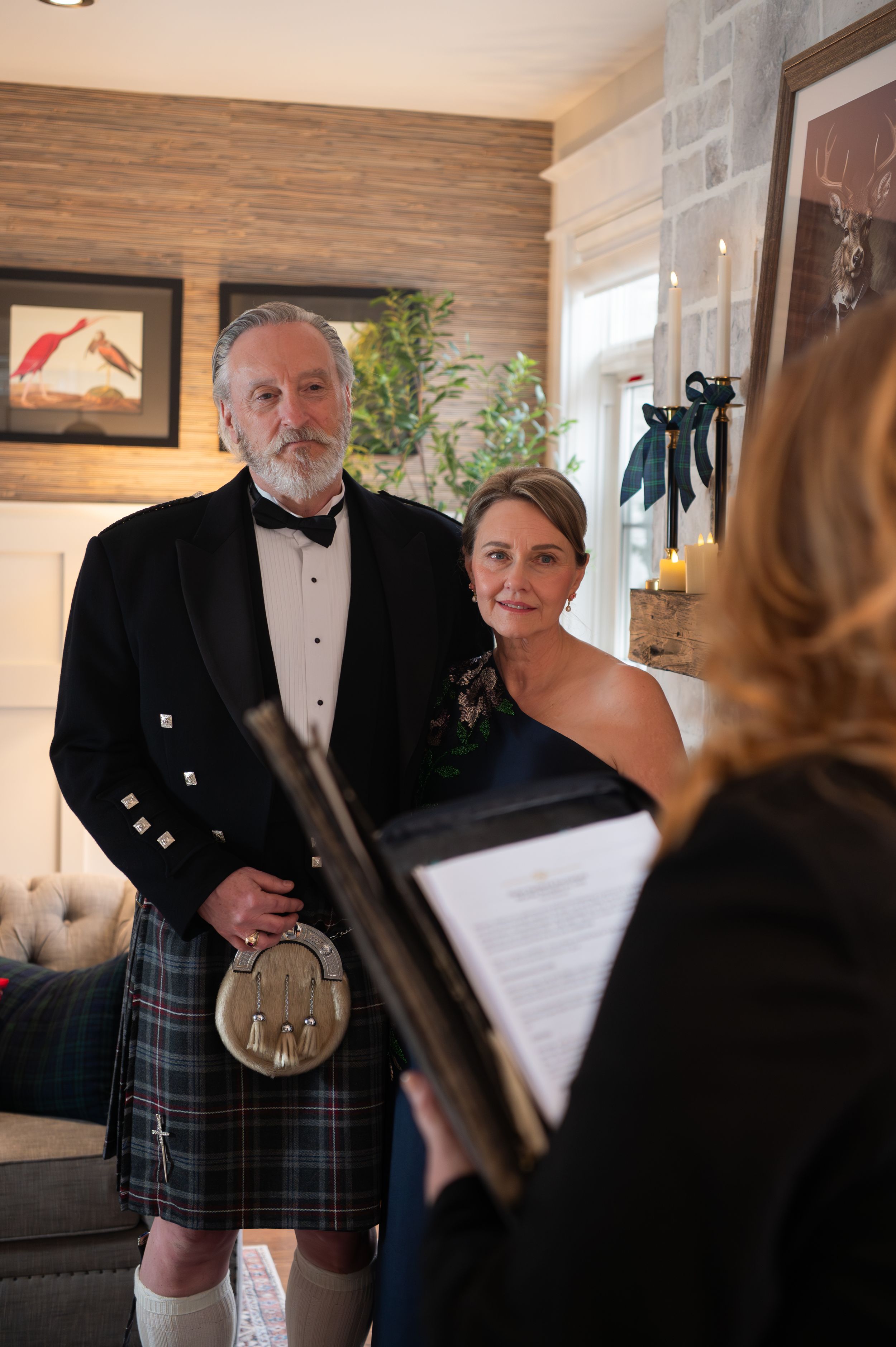 A formal ceremony takes place in a cozy room with wood-paneled walls and a person wearing a traditional Scottish kilt.