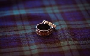 Wedding rings displayed on a blue and green plaid tartan fabric with elegant details.