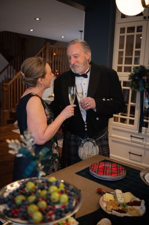 A couple in formal attire share a toast and conversation at an elegant dinner party with Scottish tartan decor.