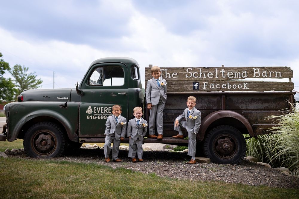 A row of vintage green trucks parked on gravel with a rustic wooden sign in the background.