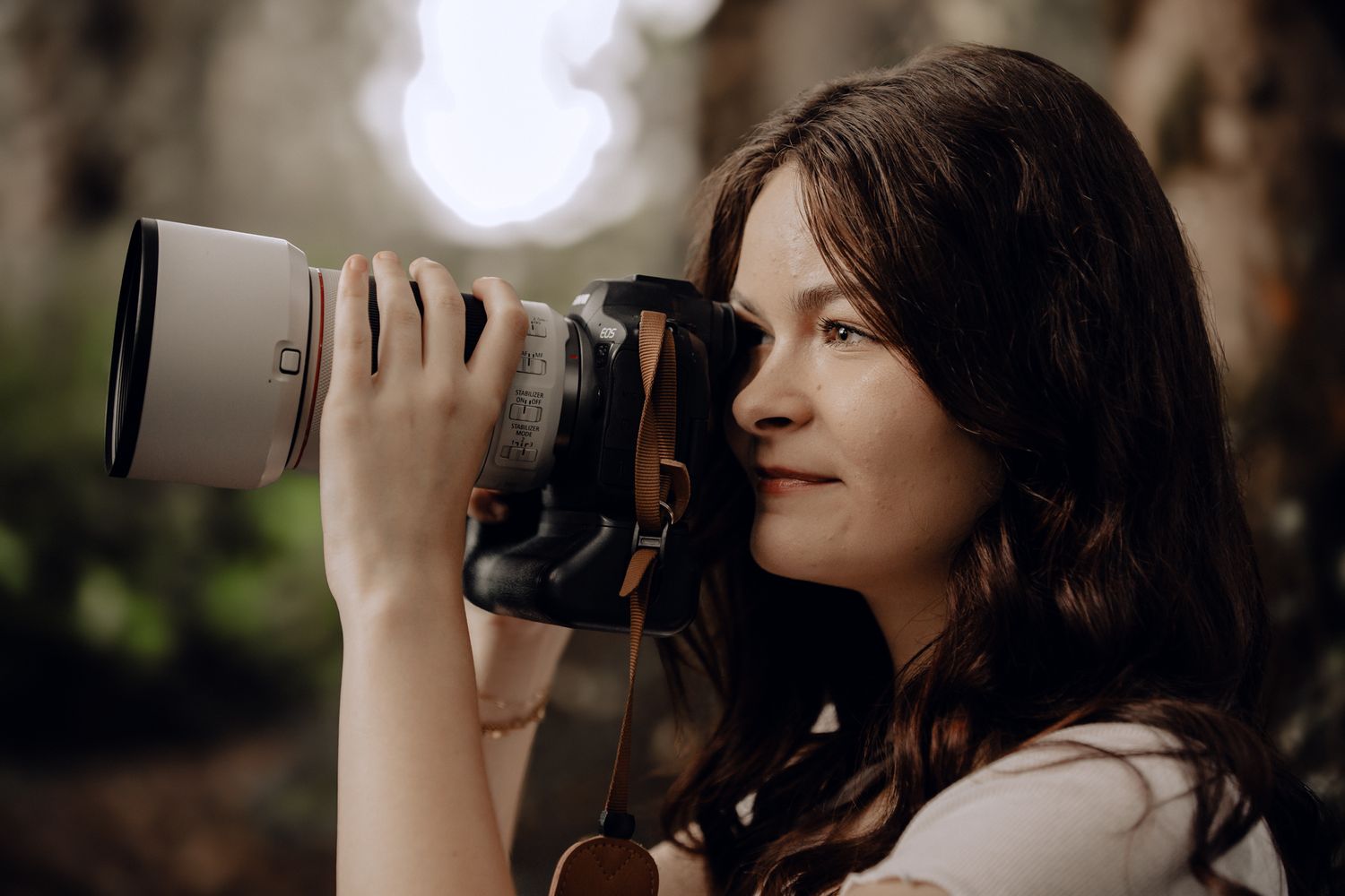 Person with dark hair photographing with a camera against a bright backlit background.