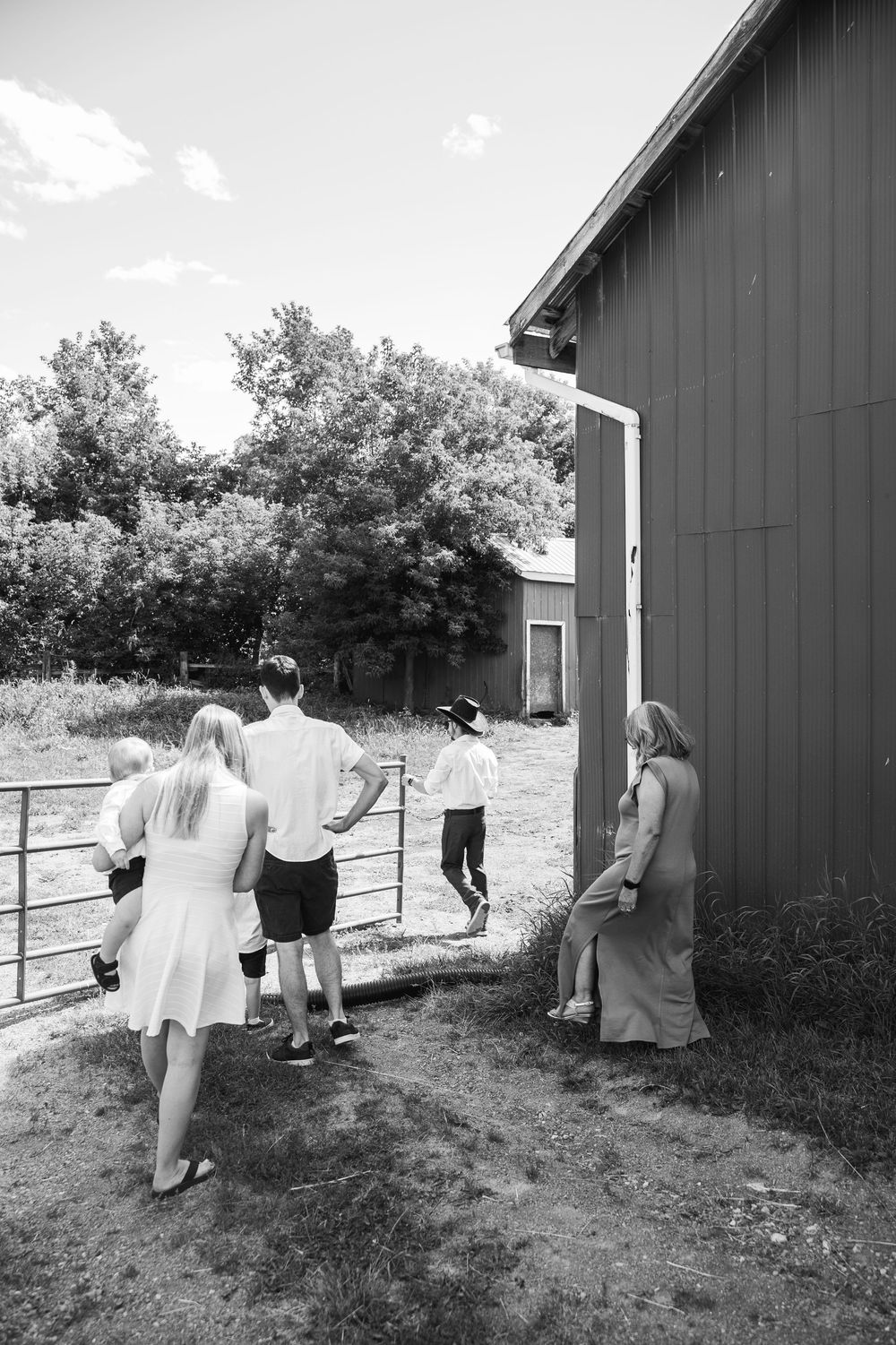 Black and white photos of people walking around the exterior of a gray barn building in a rural setting.