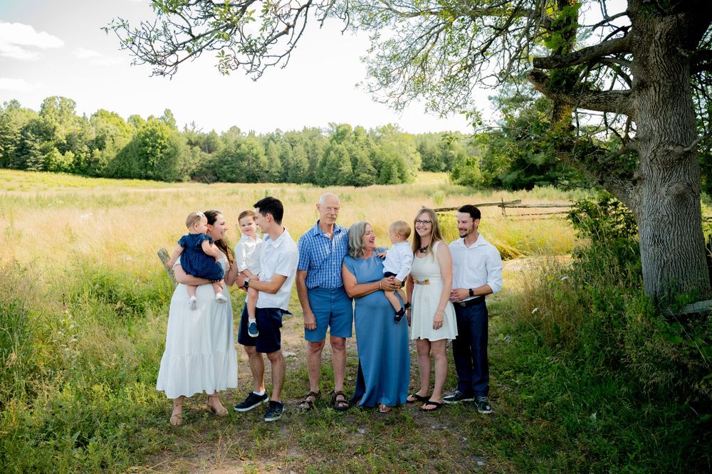 A group of people gather in a scenic meadow at golden hour for outdoor portraits in casual summer attire.