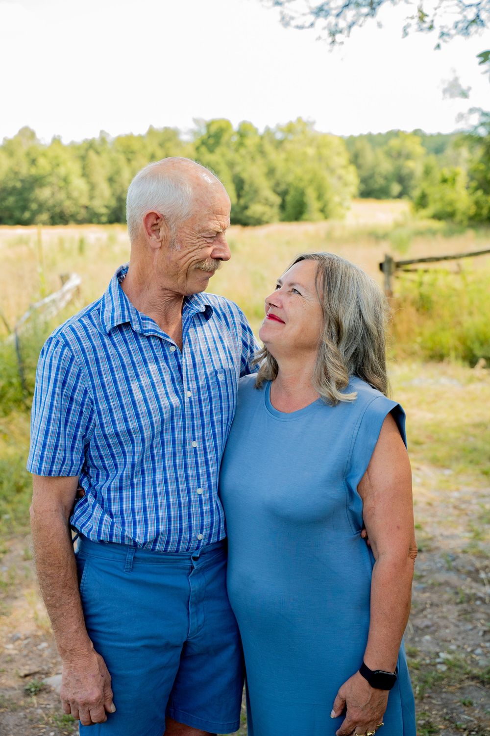 A couple in coordinating blue outfits share tender moments together in a sunny outdoor setting.