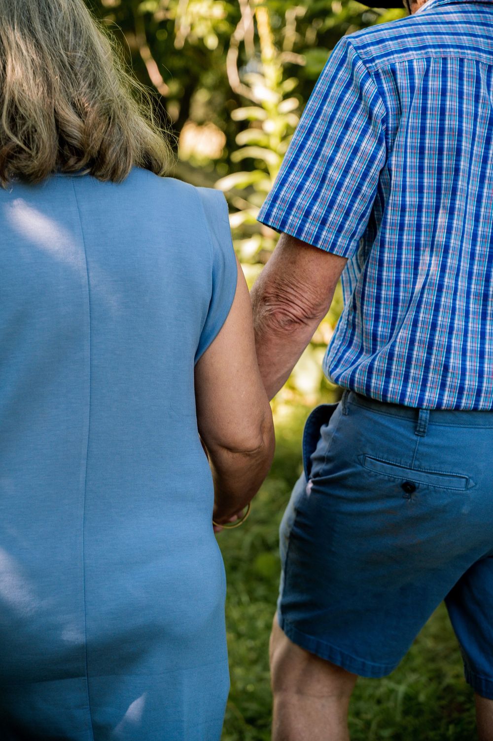 Close-up series of a couple holding hands while wearing blue plaid shirt and dress against a natural background.