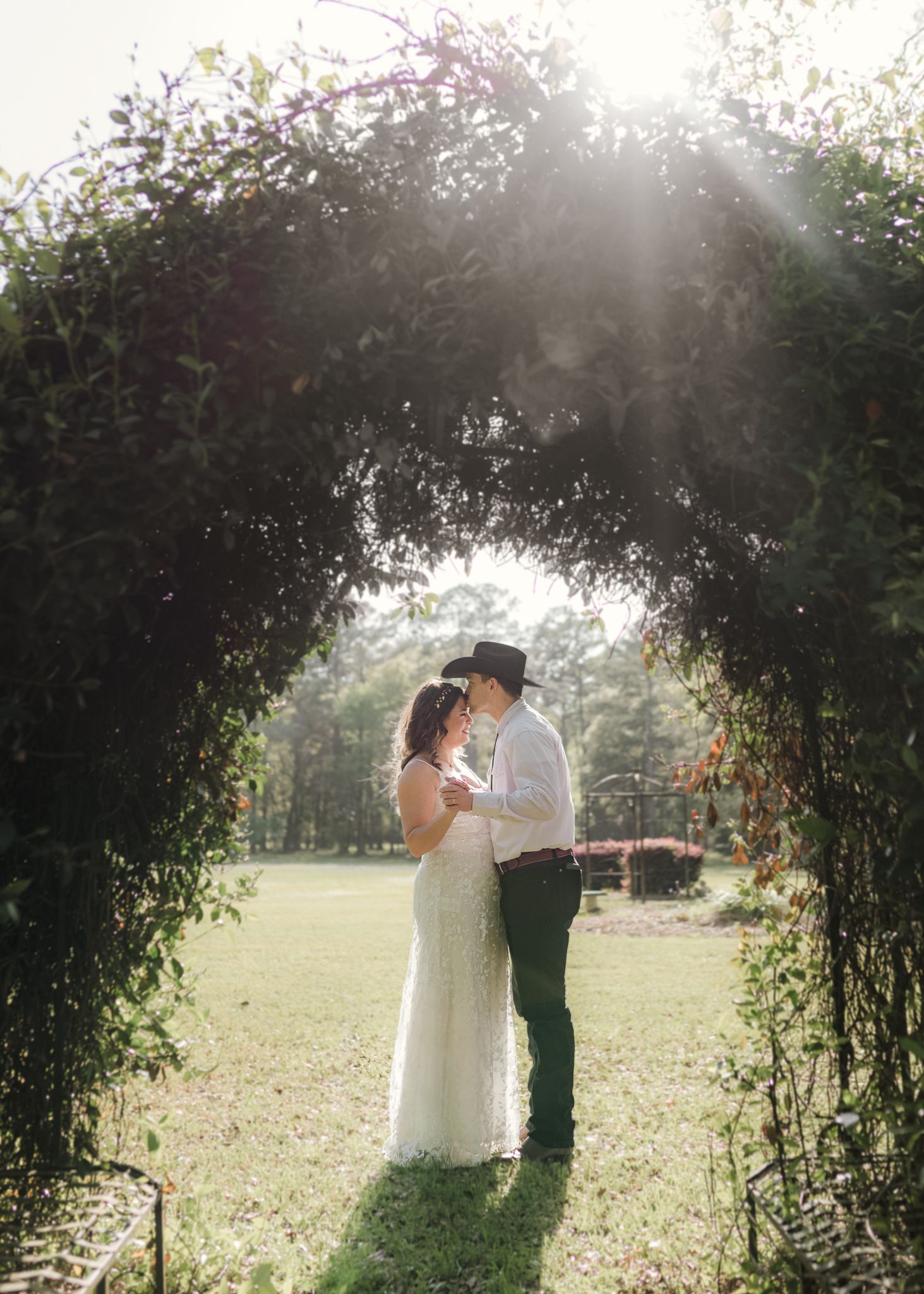 A couple shares a romantic kiss under a lush garden archway during their outdoor wedding ceremony.