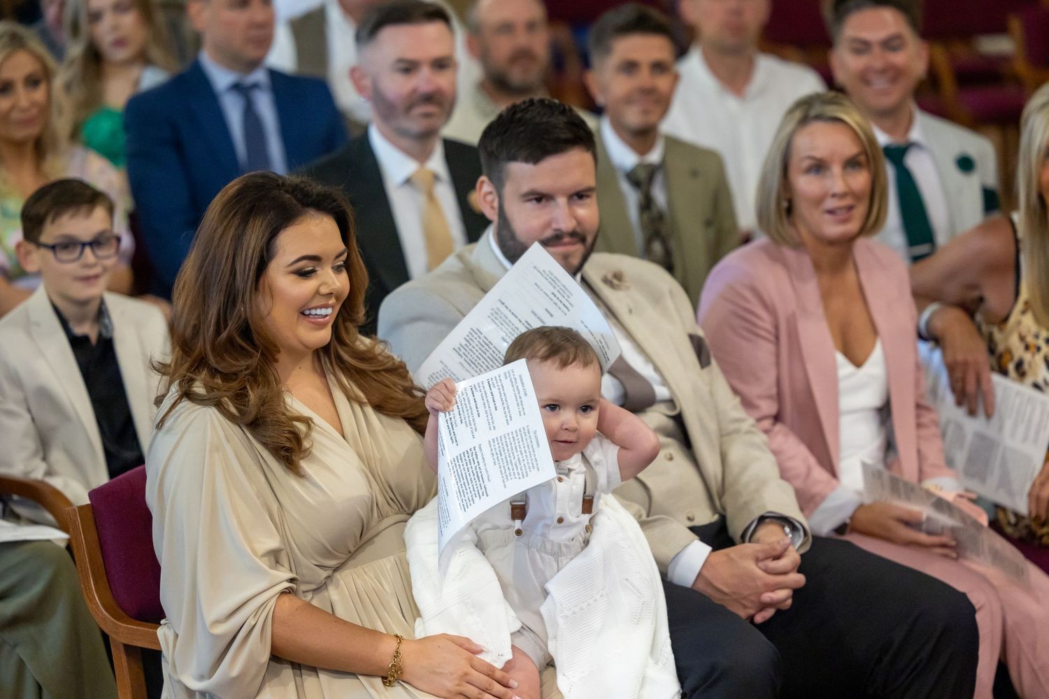Scarlett Moffatt and her fiance share a tender moment with their baby during a church ceremony in formal attire.