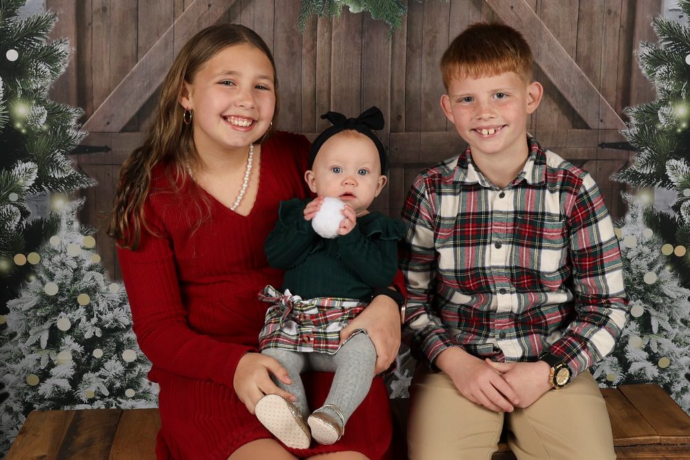 Holiday portrait session in front of decorated Christmas trees and wooden backdrop.