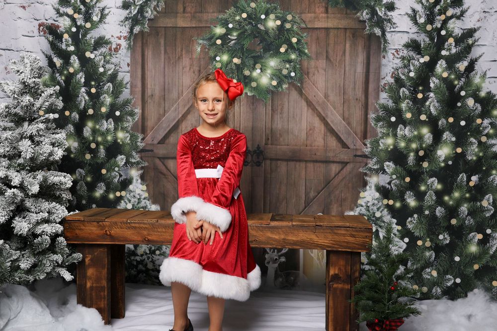 Holiday scene with snow-covered evergreen trees and wooden bench against rustic barn door.