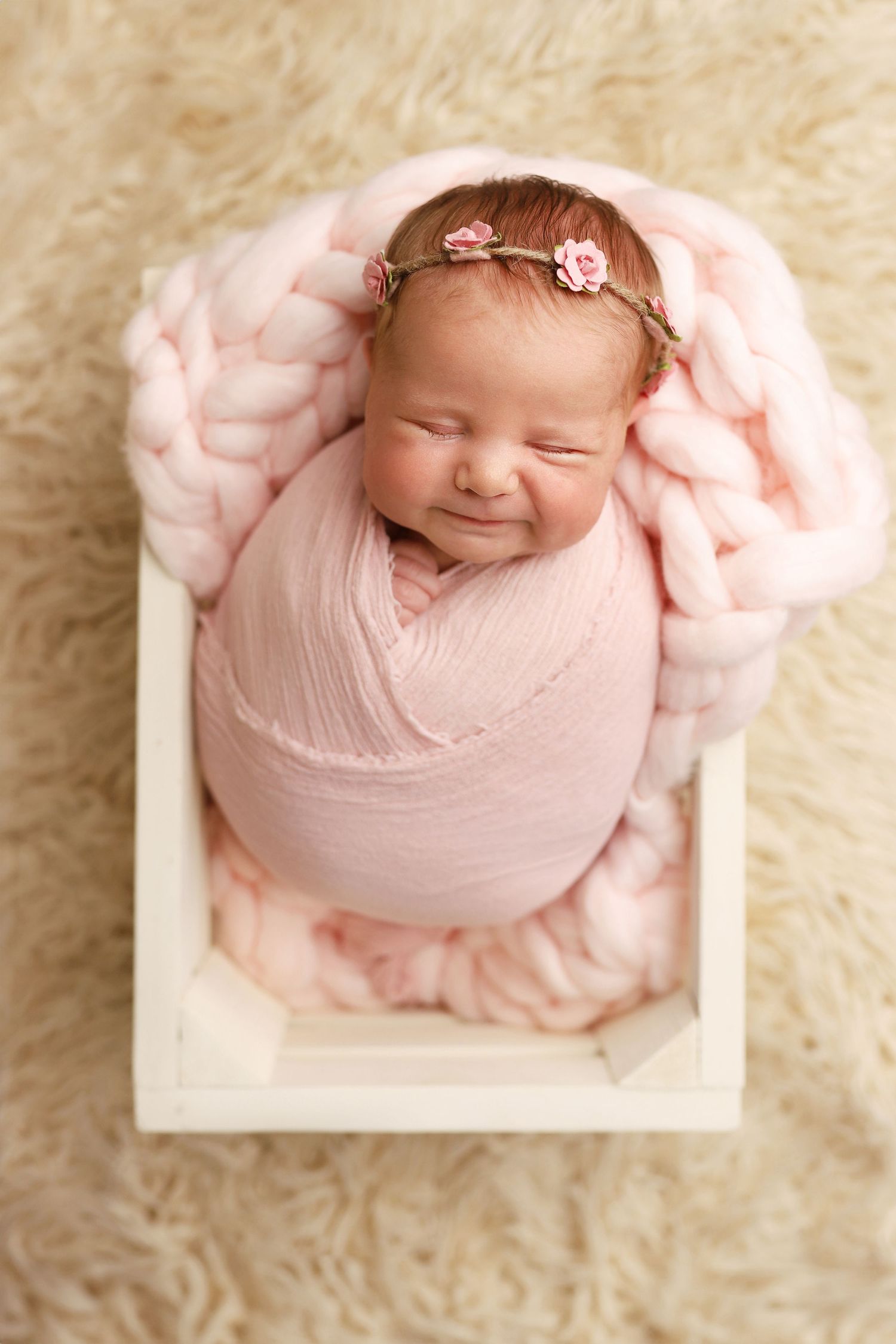 Sweet newborn photography session featuring a sleeping baby wrapped in soft pink fabric on cream-colored fur backdrop.