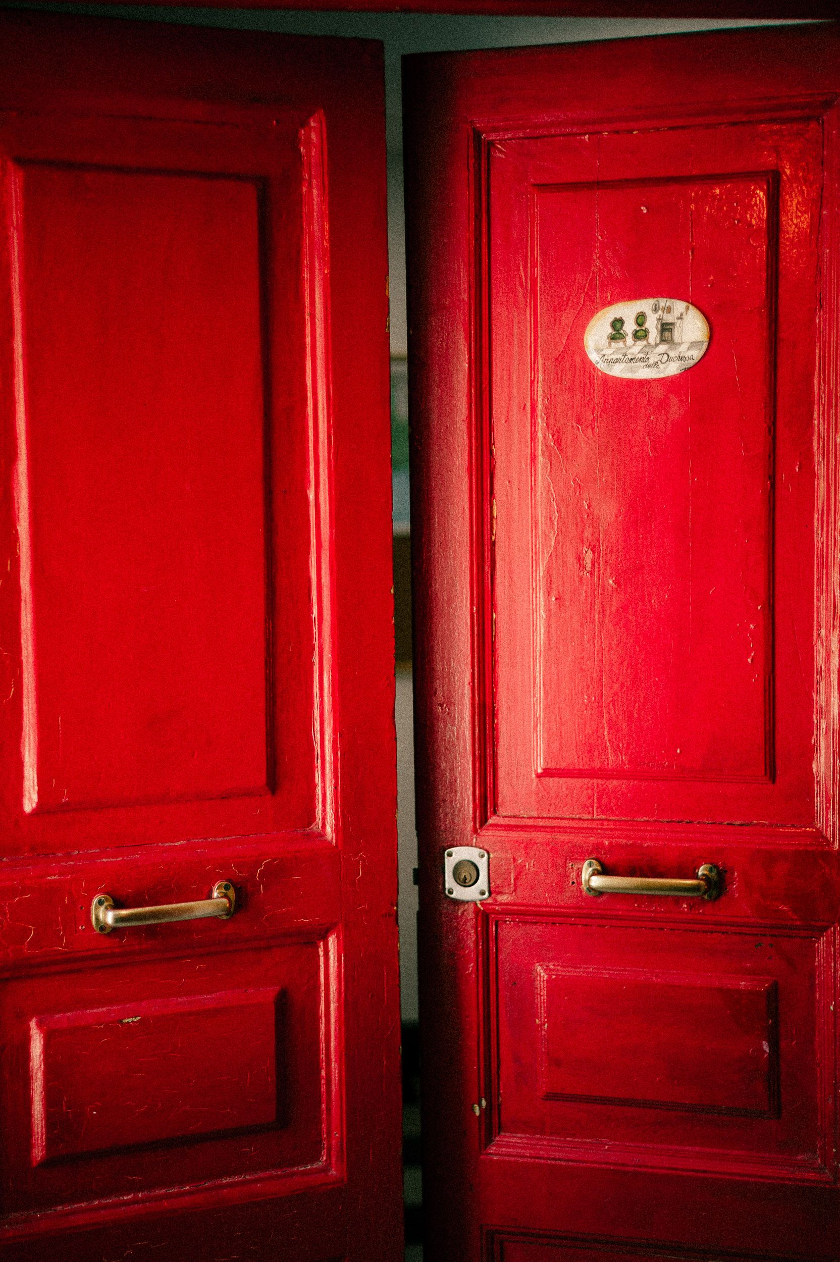 A row of bright red wooden doors with brass handles in a vintage hallway creates a striking architectural pattern.