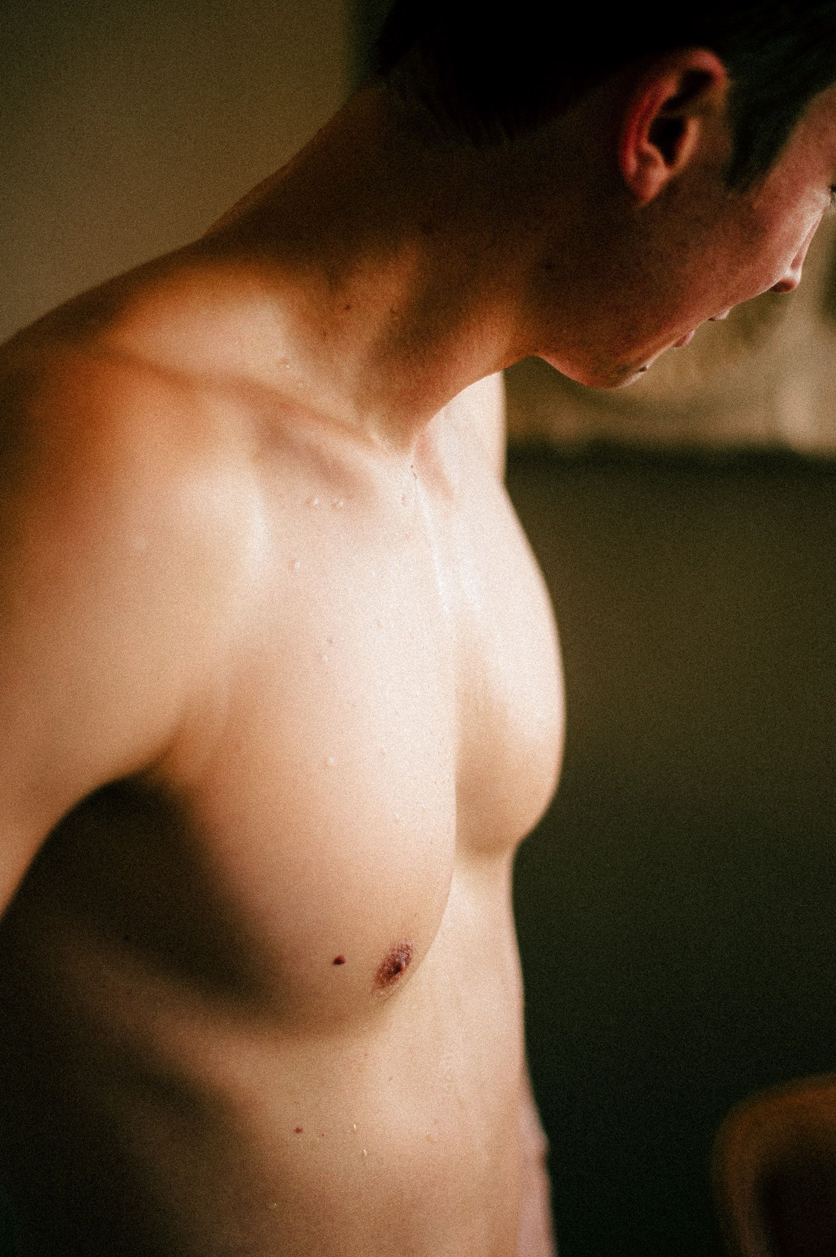 Close-up artistic black and white photograph showing bare torso in dramatic lighting and shadows.