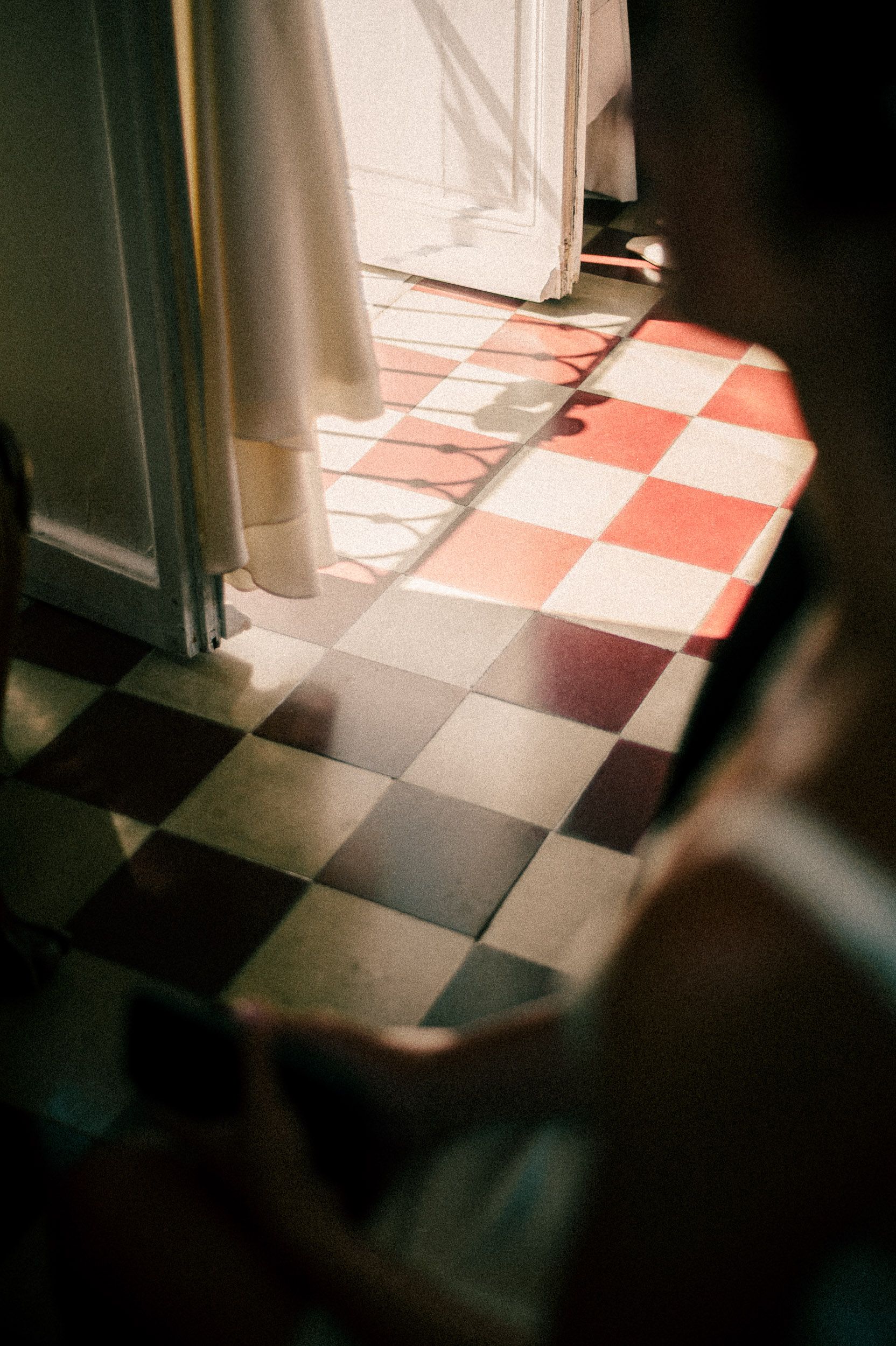 Sunlight creates dramatic shadows on a pink and white checkered tile floor in an interior space.