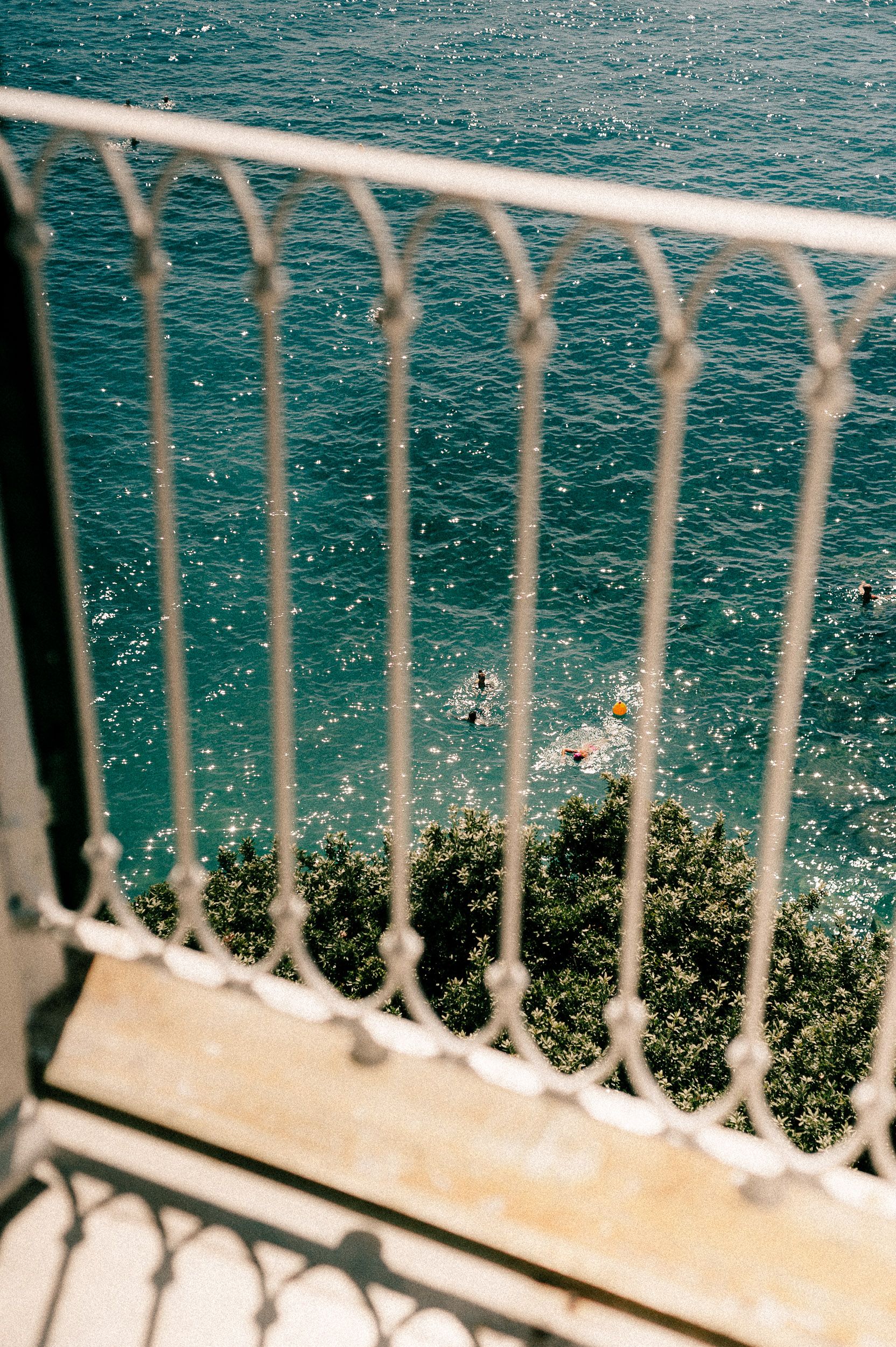 White metal railing overlooking turquoise Mediterranean waters with coastal vegetation visible below.