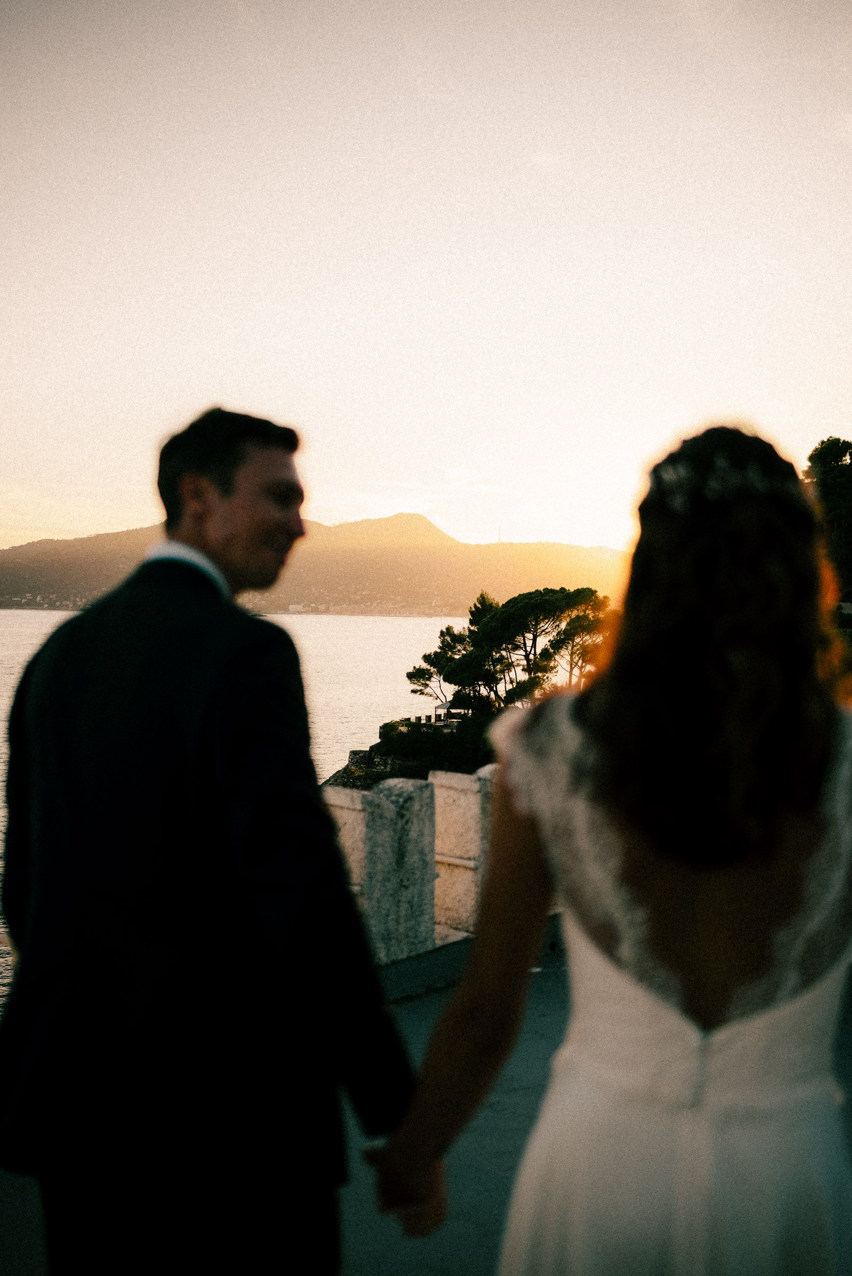 Romantic silhouettes of a couple against sunset sky in panoramic wedding photos by the ocean.