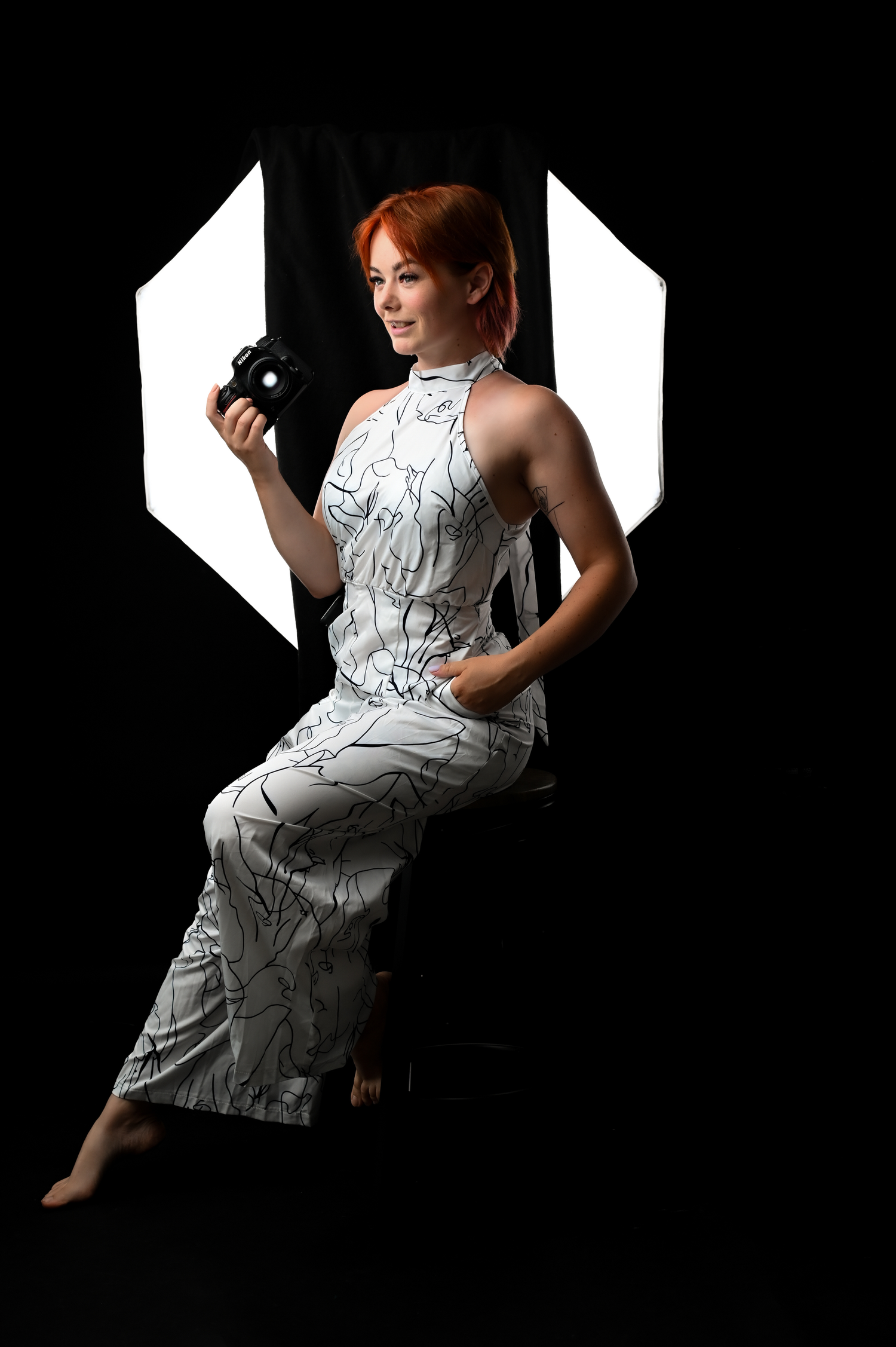 A figure in a white patterned dress poses against a dark background in an artistic photo series.