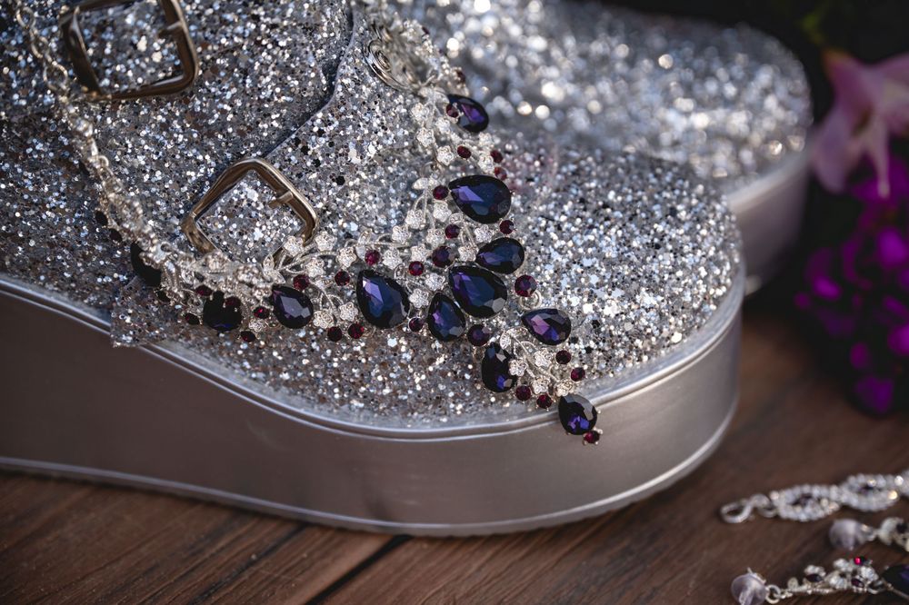 Elegant dark blue and crystal necklace displayed on a glittery silver surface with purple flowers in the background.