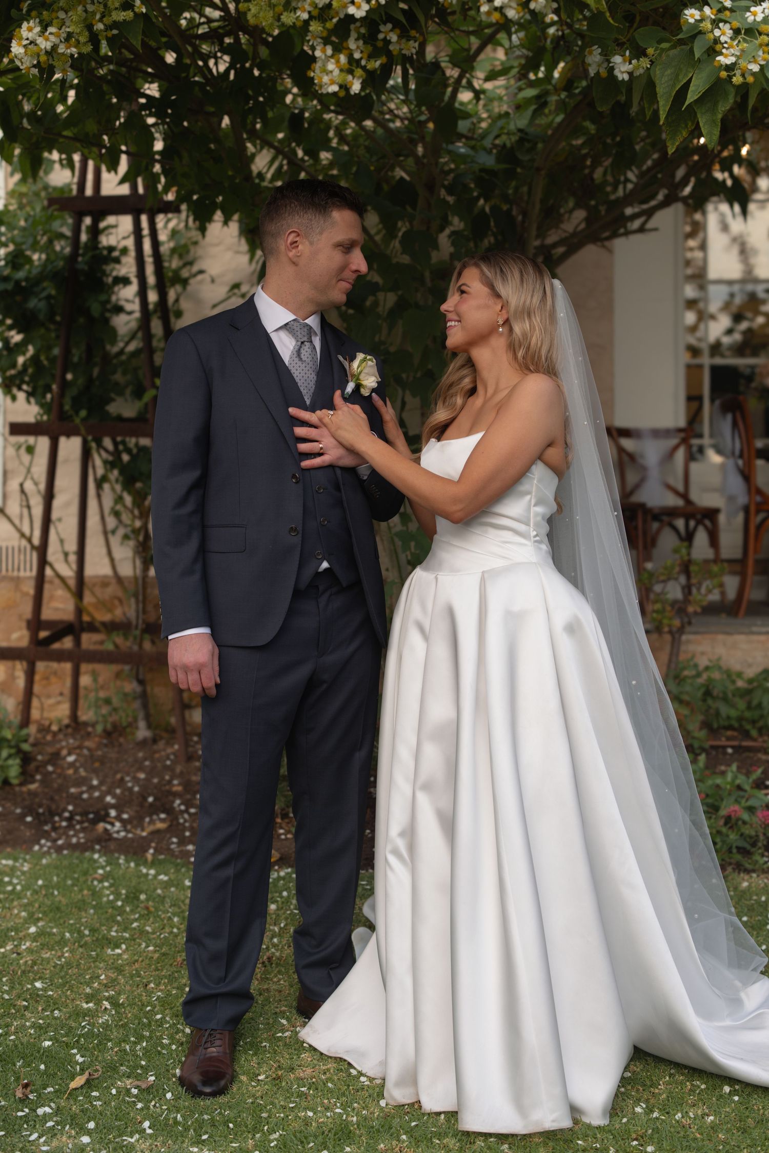 A bride and groom share an intimate moment in a garden setting with lush greenery in the background.