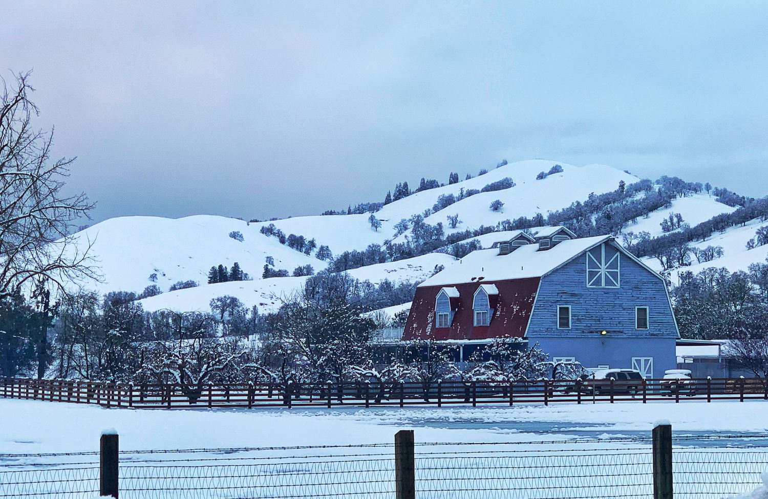 Snow-covered mountains and fenced pastures create a serene winter panorama in a rural valley.