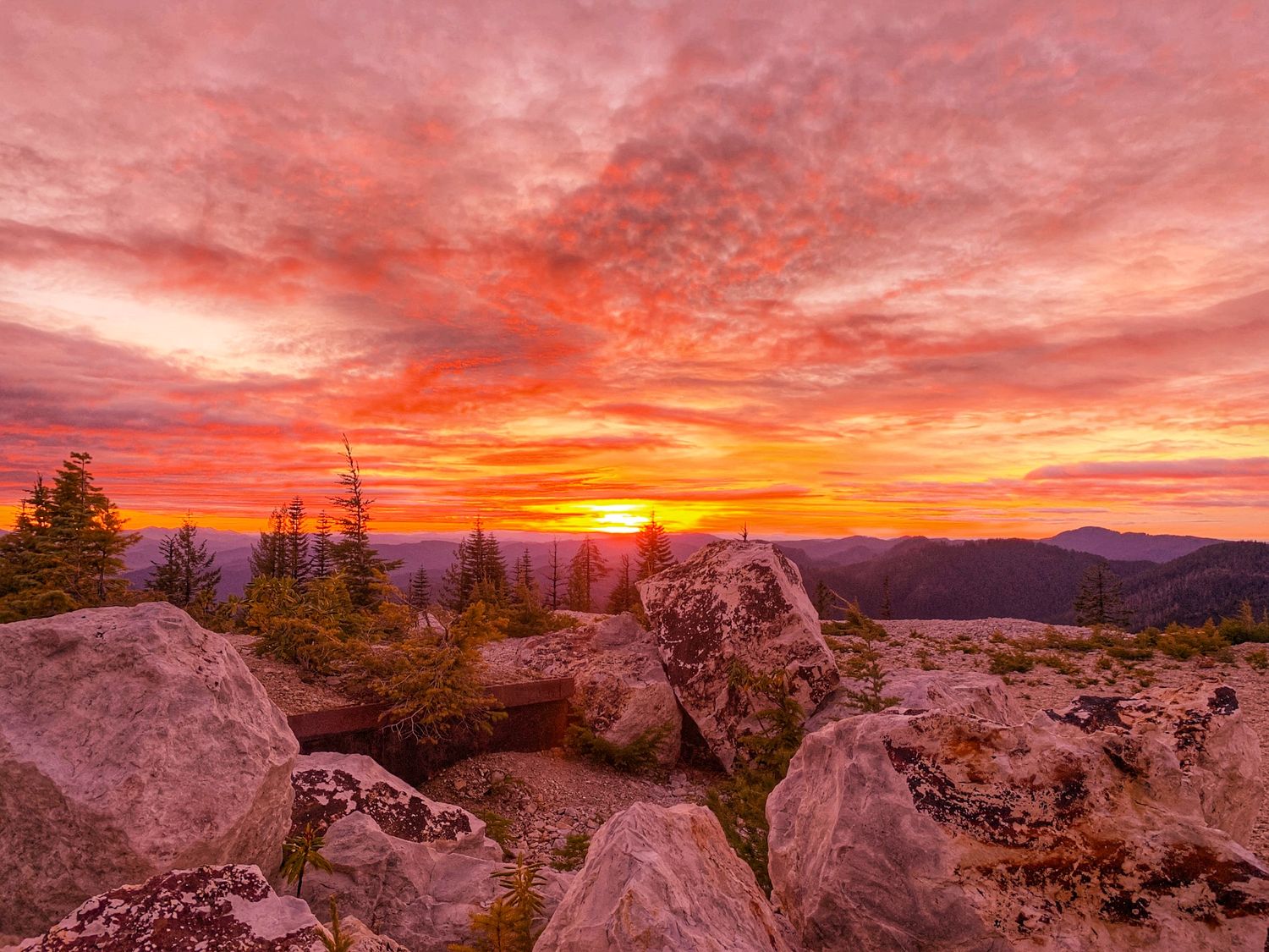 Rocky mountain summit at sunset with dramatic red and orange clouds painting the horizon.