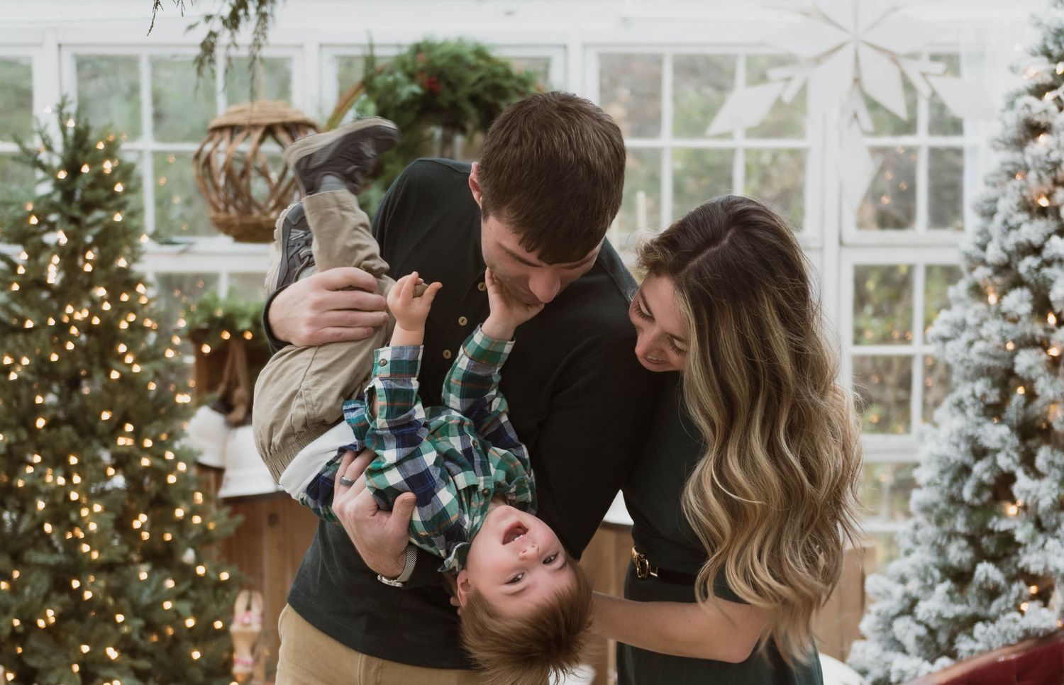 A playful family moment in front of a Christmas tree with a child being held upside down.