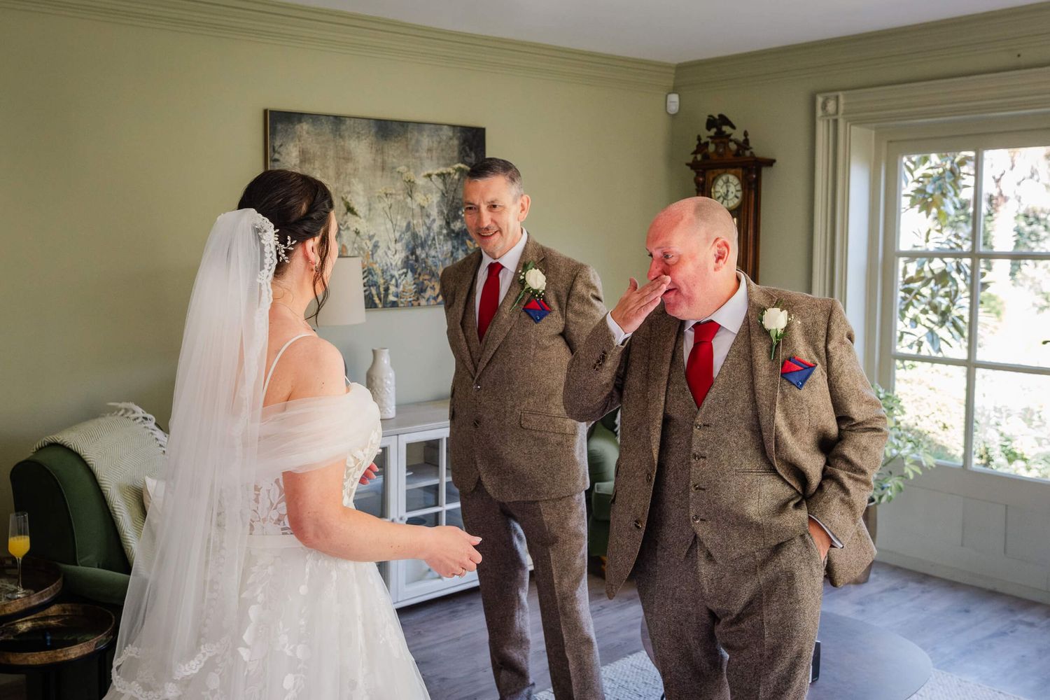 Wedding party members share emotional reactions during a first look moment in a bright indoor setting.