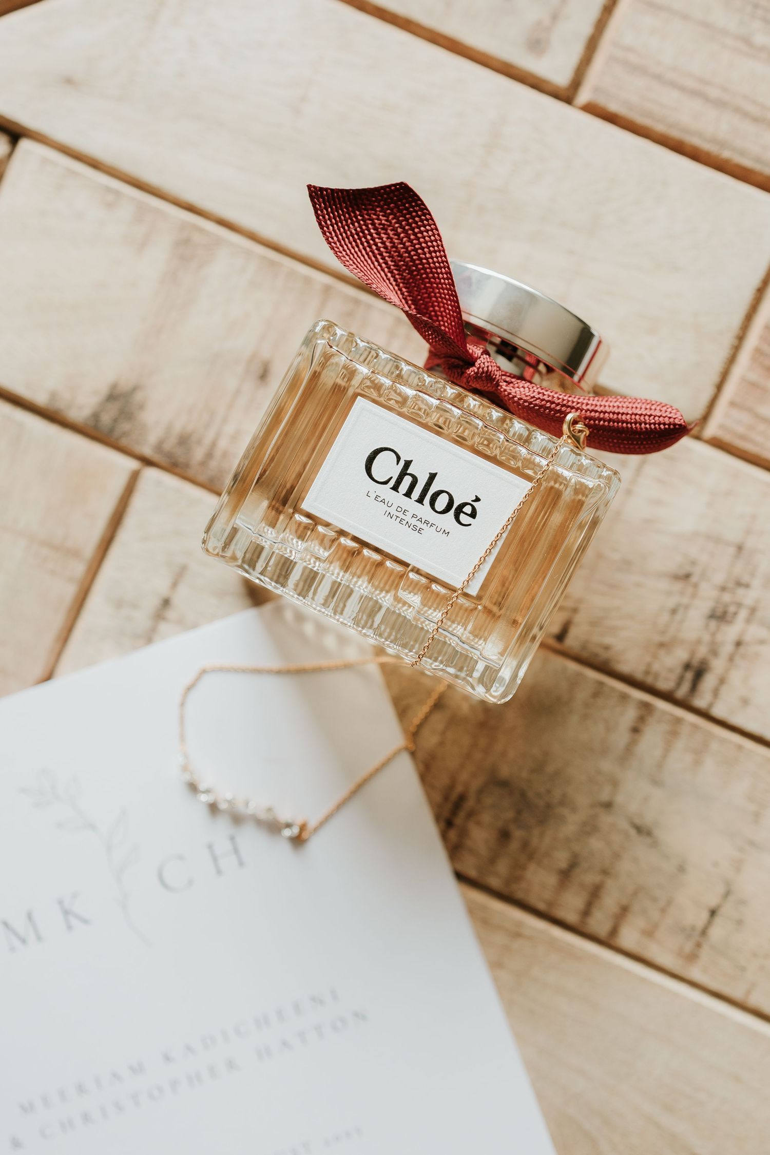 Elegant Chloe perfume bottle with red ribbon displayed on white wooden surface against neutral background.
