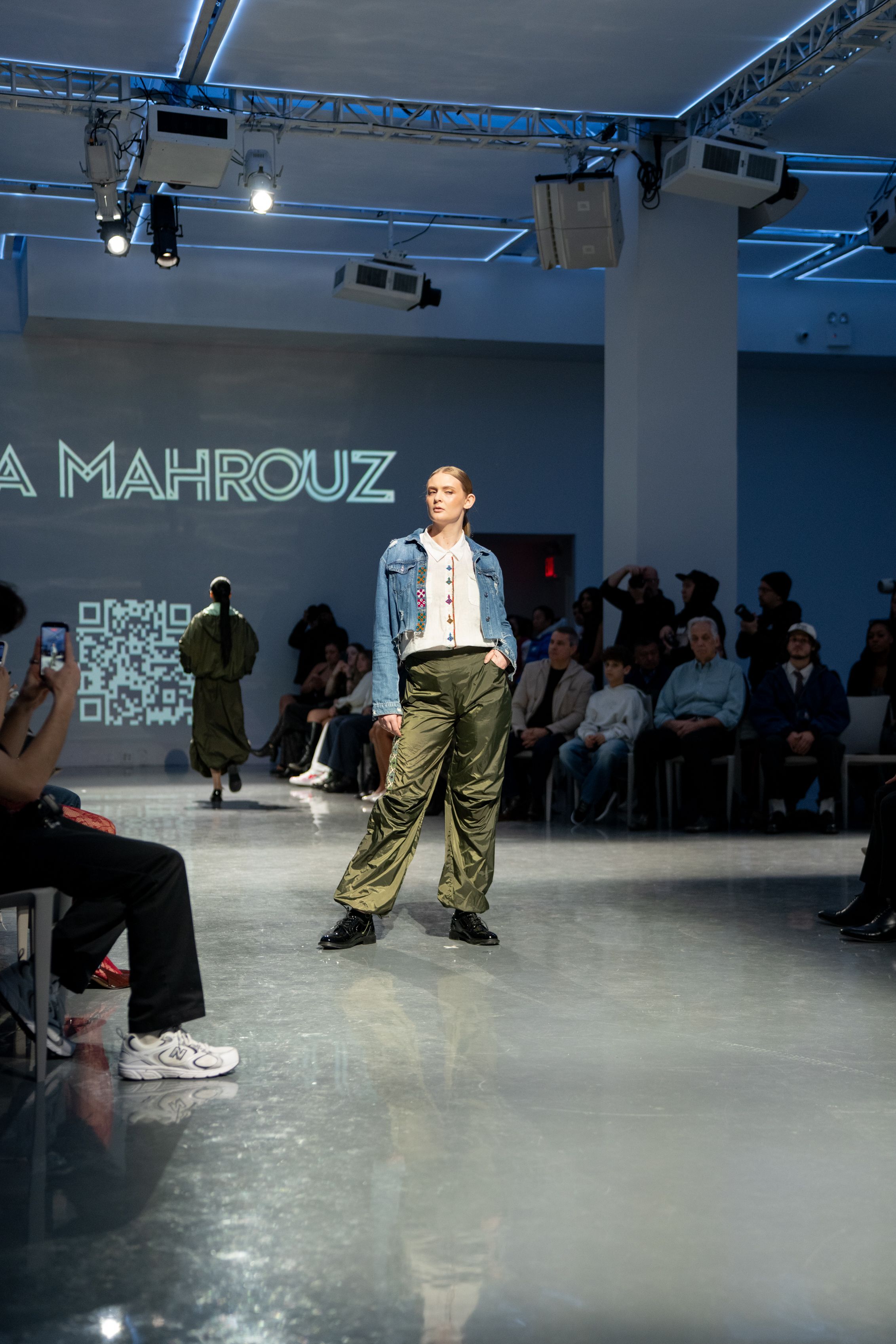 Model walks the runway at Ia Mahrouz fashion show wearing olive cargo pants and denim jacket.