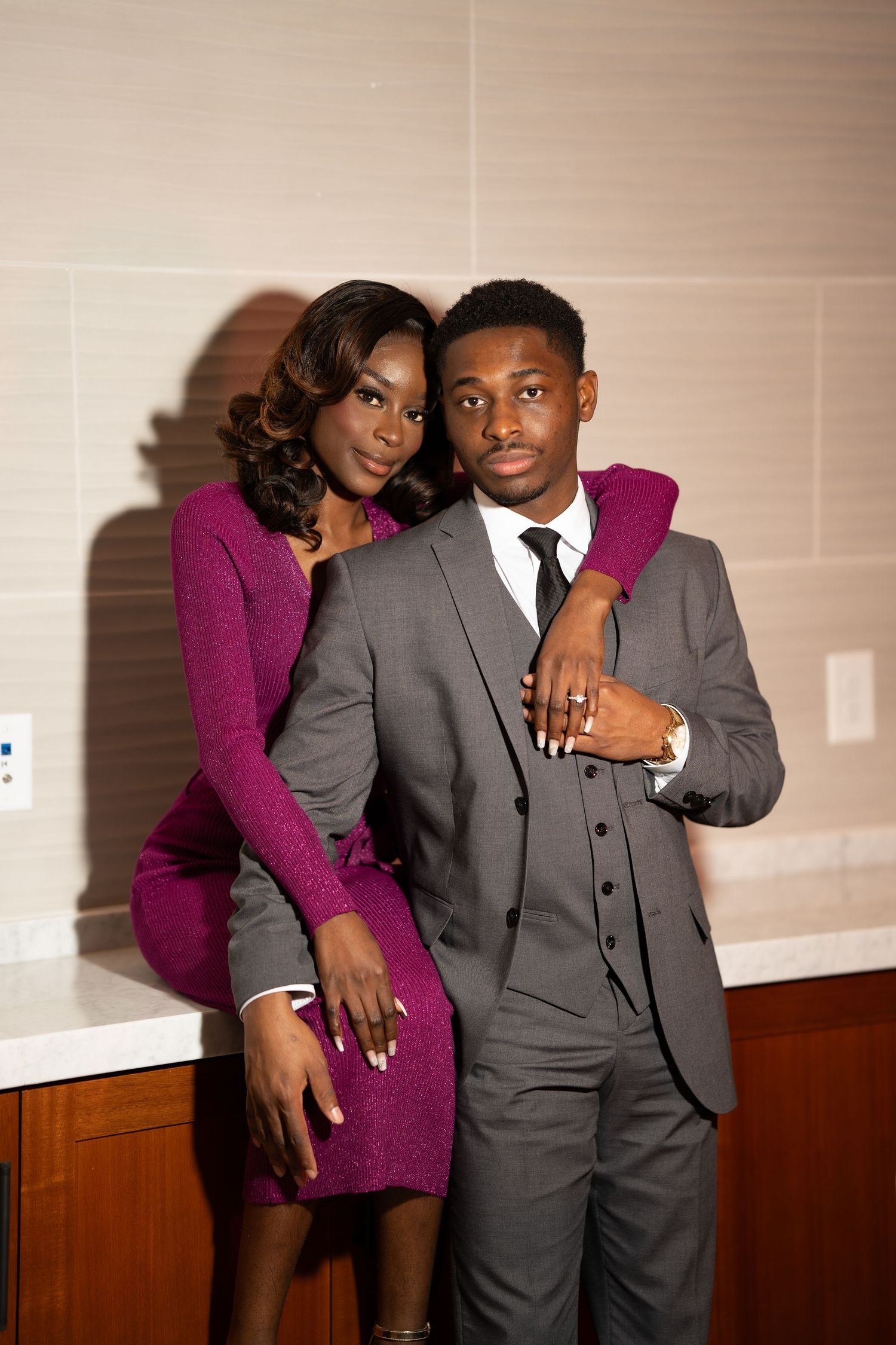 A couple poses together in formal attire, with someone wearing a purple dress and another in a gray suit.