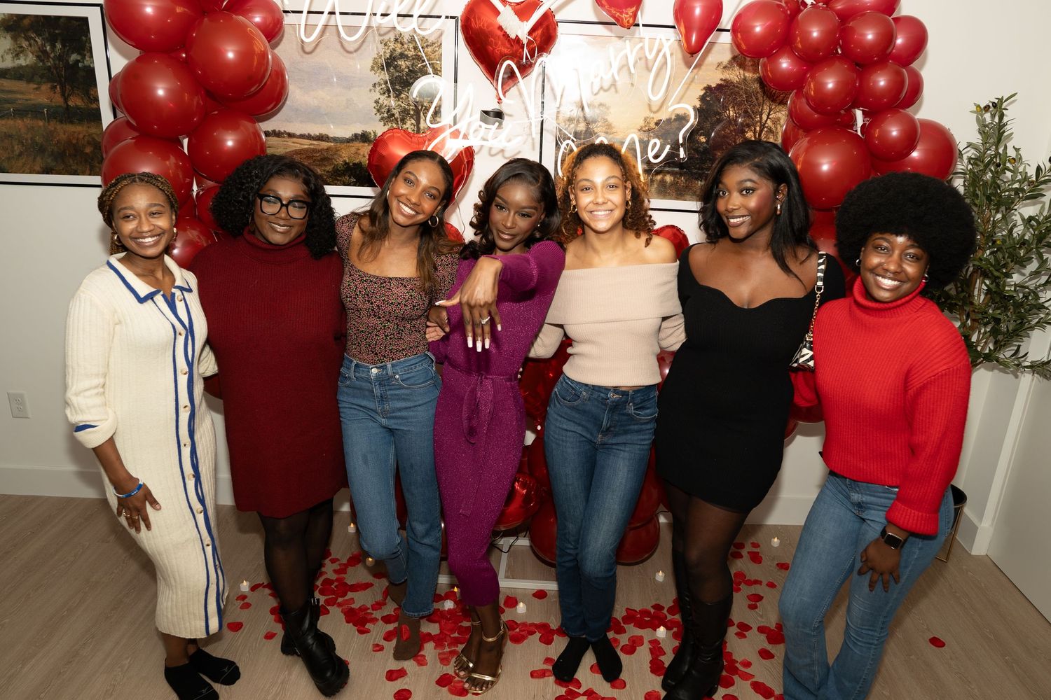A group poses together at a party decorated with red balloons and festive decorations.
